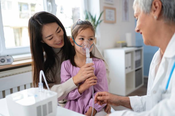 In the ordination, while sitting in her mother lap, Japanese girl receiving a treatment with nebulizer, from the senior Caucasian female pediatrician